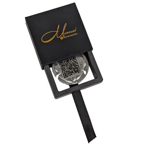 May include: A black box with the text "Memorial Audiobiography" on the top. The box is open and a silver disc with a QR code and the text "Audiobiography" is visible inside.