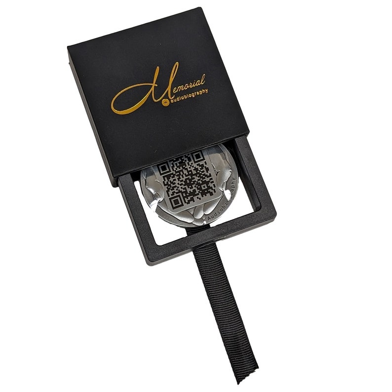 May include: A black box with the text "Memorial Audiobiography" on the top. The box is open and a silver disc with a QR code and the text "Audiobiography" is visible inside.