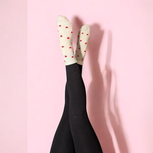 May include: A pair of black leggings with white socks that have red hearts printed on them. The socks are pulled up to the knees and the legs are crossed at the ankles.
