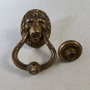 Peut inclure: Un heurtoir de porte en laiton avec un motif de tête de lion. Le heurtoir a une poignée en forme d'anneau et un bouton rond séparé.