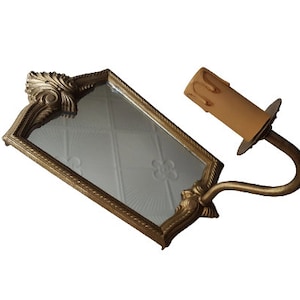 May include: A gold-toned wall sconce with a small mirror and a candle-style light bulb. The mirror has a decorative frame and the sconce has a curved arm.