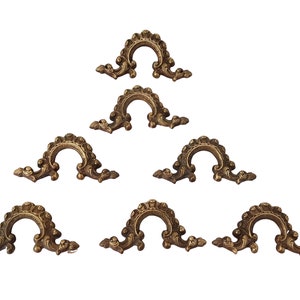 May include: Set of seven ornate gold-toned metal decorative accents. Each accent features a curved, arched design with intricate scrollwork and floral details.