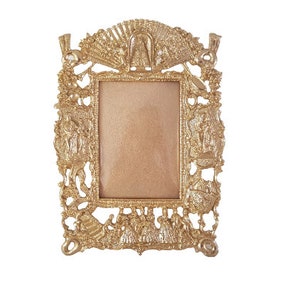 May include: A gold-toned metal picture frame with an ornate design. The frame has a rectangular opening for a photo and features intricate details around the edges.
