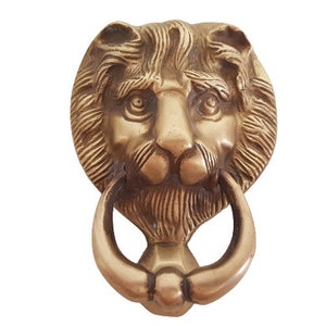 May include: A gold lion's head door knocker with a ring handle. The knocker is detailed with a textured mane and facial features.