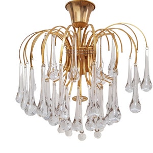 May include: A gold-toned chandelier with clear glass teardrop-shaped pendants. The chandelier has a circular base and multiple arms that curve upwards.