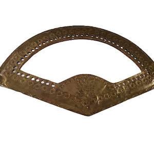 May include: A gold-colored metal frame with a decorative design. The frame is shaped like a half-circle and has a scalloped edge.