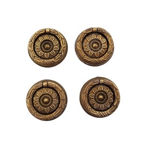 Könnte beinhalten: Vier goldfarbene runde Schrankknöpfe mit floralem Design. Jeder Knopf hat einen Ring zum Ziehen.