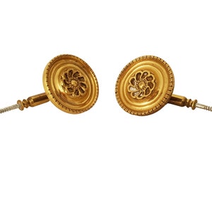 May include: Two gold-toned metal curtain tiebacks with a decorative floral design. Each tieback has a screw for mounting.