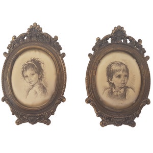 May include: Two oval framed portraits of children. The frames are ornate and gold in color. The portraits are in black and white and depict a girl and a boy.