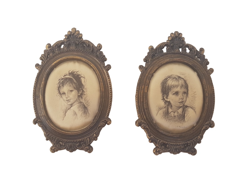 May include: Two oval framed portraits of children. The frames are ornate and gold in color. The portraits are in black and white and depict a girl and a boy.