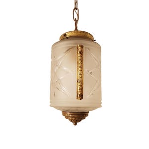 Peut inclure: Un luminaire suspendu en verre givré avec une structure et une chaîne en métal doré. Le verre présente un motif géométrique et la structure est ornée de détails décoratifs.