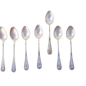 Könnte beinhalten: Satz von sieben silbernen Löffeln mit verzierten Griffen. Die Löffel sind in einer Reihe angeordnet, wobei die Griffe zum Betrachter zeigen.