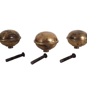 Pode incluir: Três remates de metal dourado com topo arredondado e base rosqueada. Cada remate é acompanhado por um parafuso preto.