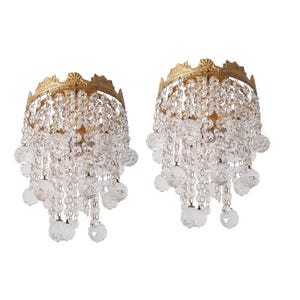 Peut inclure: Deux appliques murales ornées avec un sommet doré en forme de couronne et des perles de cristal transparentes en cascade. Les appliques sont conçues pour accueillir des luminaires, ajoutant une touche d'élégance.