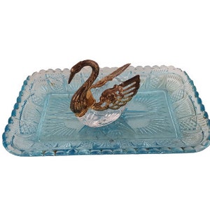 Könnte beinhalten: Ein blaues Serviertablett aus Glas mit einem dekorativen Schwanendesign. Der Schwan ist aus klarem Glas mit goldenen Akzenten.