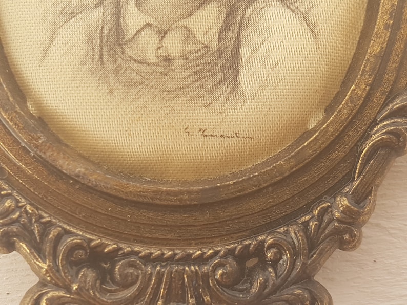 May include: A framed drawing of a person in a gold-colored ornate frame. The drawing is on a cream-colored fabric and is signed "F. Vannetten".