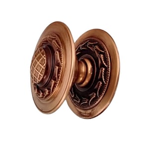 Op de afbeelding: Een paar antieke deurknopjes met een koperen afwerking. De knoppen hebben een decoratief ontwerp met een reliëfpatroon rond de randen.