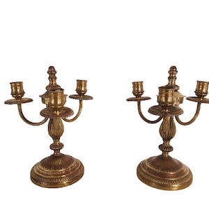 May include: A pair of antique brass candle holders with three arms each. The candle holders have a fluted design and a round base.