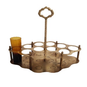 May include: A gold-toned metal bottle holder with a handle and eight individual slots for bottles. The holder has a decorative, scalloped edge.