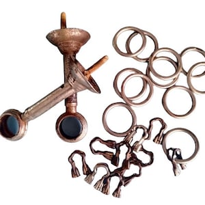 Può includere: Un set di anelli per tende in ottone antico con terminali decorativi. Gli anelli sono di diverse dimensioni e sono disposti in una pila. Ci sono anche due supporti per bastone per tende in metallo con un terminale decorativo su ciascuno.