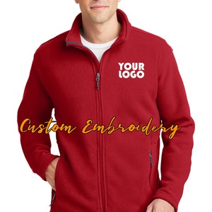 May include: A red fleece jacket with a zipper closure and two front pockets. The jacket has a gray collar and a white embroidered logo that says "YOUR LOGO".