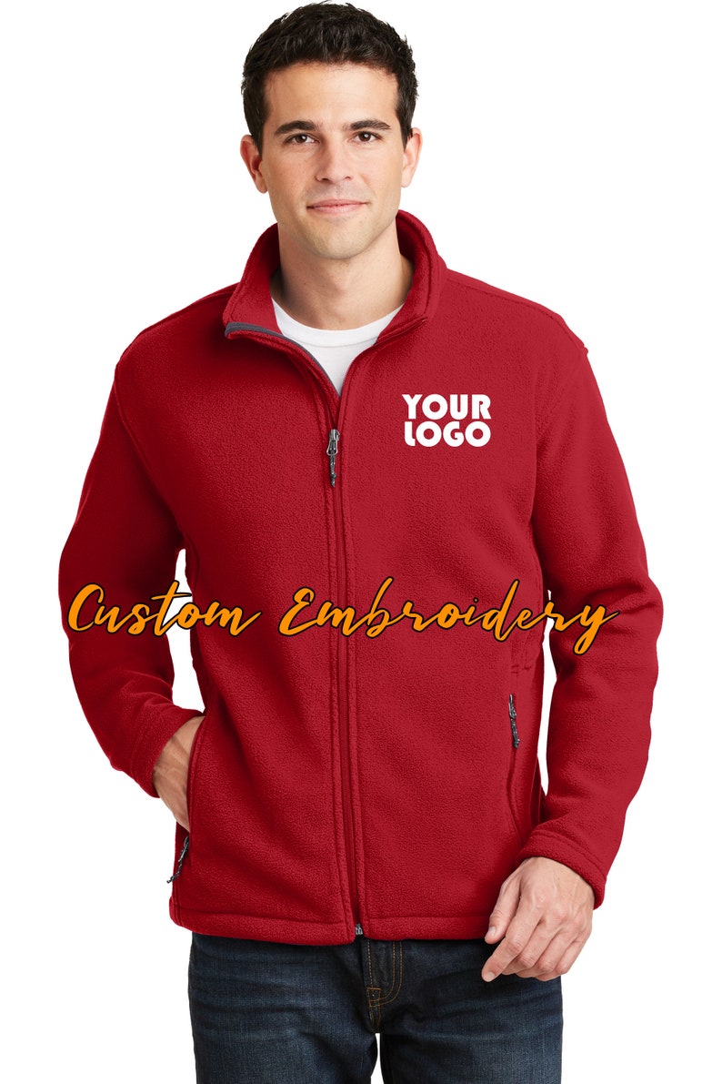 May include: A red fleece jacket with a zipper closure and two front pockets. The jacket has a gray collar and a white embroidered logo that says "YOUR LOGO".