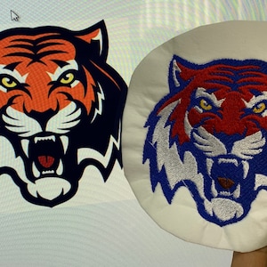 May include: A close-up of a tiger face embroidered patch. The tiger has orange, red, white, and blue fur. The patch is on a white background.