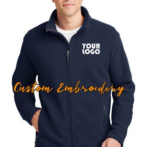 May include: A navy blue fleece jacket with a zipper closure and two front pockets. The jacket has a white embroidered logo that says "YOUR LOGO" on the left chest.