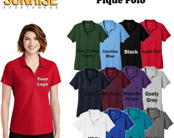 May include: A selection of women's pique polo shirts in various colors, including deep forest green, carolina blue, black, apple red, navy, maroon, majestic purple, gusty grey, white, true royal, teal, and sterling grey. The shirts feature a classic polo design with a button-down collar and short sleeves. The text "Your Logo" is embroidered on the left chest of one of the shirts.