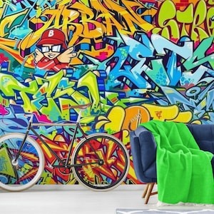 Puede incluir: Un colorido mural de graffiti con un personaje de dibujos animados con gorra roja y gafas. Una bicicleta negra con ruedas con llantas blancas est&aacute; frente al mural. Un sof&aacute; azul con una manta verde est&aacute; a la derecha de la imagen.