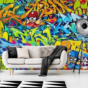 Puede incluir: Un vibrante mural de graffiti en tonos amarillos, naranjas, azules y verdes domina la pared detr&aacute;s de un sof&aacute; blanco. La obra de arte presenta letras estilizadas y figuras de dibujos animados. Una alfombra geom&eacute;trica en blanco y negro est&aacute; en el suelo.