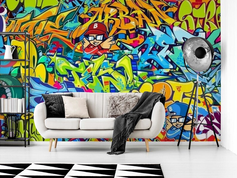 Puede incluir: Un vibrante mural de graffiti en tonos amarillos, naranjas, azules y verdes domina la pared detr&aacute;s de un sof&aacute; blanco. La obra de arte presenta letras estilizadas y figuras de dibujos animados. Una alfombra geom&eacute;trica en blanco y negro est&aacute; en el suelo.