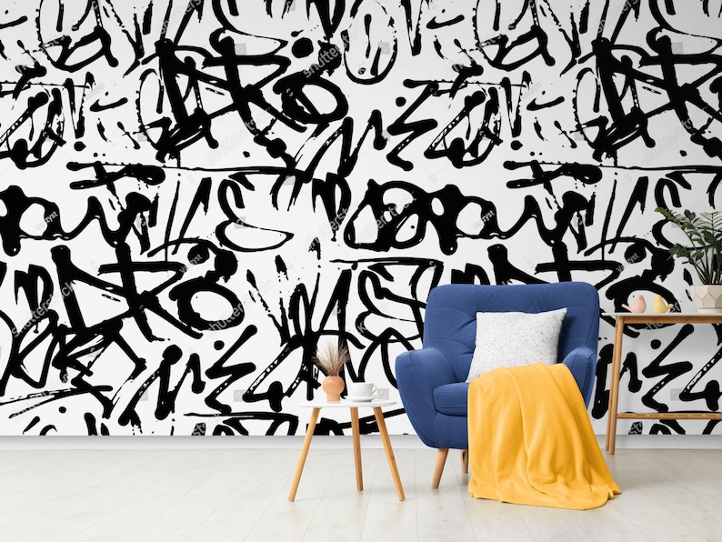 May include: A blue armchair with a yellow throw blanket sits in front of a wall with a black and white graffiti pattern. A small wooden table with a white cup sits next to the chair.