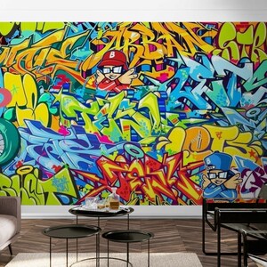 Puede incluir: Un vibrante mural de graffiti con letras abstractas coloridas y personajes de dibujos animados. La obra de arte utiliza una paleta de azules, amarillos, naranjas y verdes. El dise&ntilde;o se aplica a una pared.