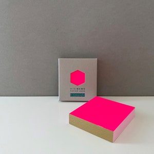 Könnte beinhalten: Ein Packung leuchtend pinkfarbenes Notizpapier mit goldfarbenem Rand. Das Papier ist in einer grauen Schachtel verpackt, auf der vorne der Text "MINIMEMO PAPIER 300G le typographe" steht.