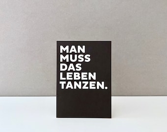 May include: Black card with white text that reads "Man muss das Leben tanzen."