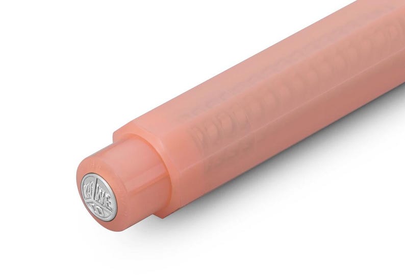 May include: Close-up of a peach-colored pen. The pen's body is a solid, matte finish, with a rounded tip. The pen's end cap features a silver emblem. The pen is angled diagonally against a white background.