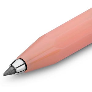 May include: Close-up of a peach-colored mechanical pencil. The pencil has a metallic silver tip and a dark gray lead. The body of the pencil is smooth and angled, with a modern design.
