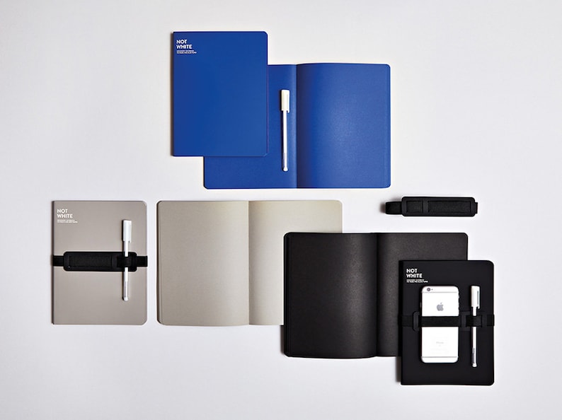 May include: An assortment of notebooks in blue, gray, and black, some open to reveal blank pages. Each notebook has a pen and a black elastic band. The text "NOT WHITE" is printed on some of the notebooks.