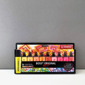 Könnte beinhalten: Eine Packung mit 10 STABILO BOSS ORIGINAL ART Y Textmarkern in verschiedenen Pastellfarben. Die Verpackung zeigt ein farbenfrohes geometrisches Design und den Text "BOSS ORIGINAL ART Y".