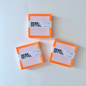 Puede incluir: Tres blocs de notas naranjas con bandas blancas y el texto "DENK-ZETTEL" están dispuestos sobre una superficie blanca. Cada bloc de notas tiene un patrón de cuadrícula y mide 7,2 x 7,2 cm. El texto está en alemán.