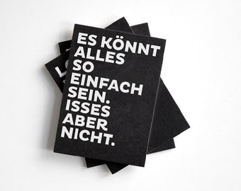 May include: A stack of black notebooks with white text that reads "Es könnt alles so einfach sein. Isses aber nicht."