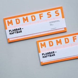 Puede incluir: Dos notas adhesivas rectangulares naranjas y blancas con el texto "MDMFSS" y "PLANBAR-HAFTBAR" en negro. Las notas tienen un patrón de cuadrícula y están sobre una superficie gris.