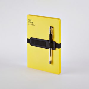 May include: A bright yellow notebook with the text "NOT WHITE" and a black elastic band holding a pen. The pen is silver and black. The notebook is a solid color and has a clean, modern design.