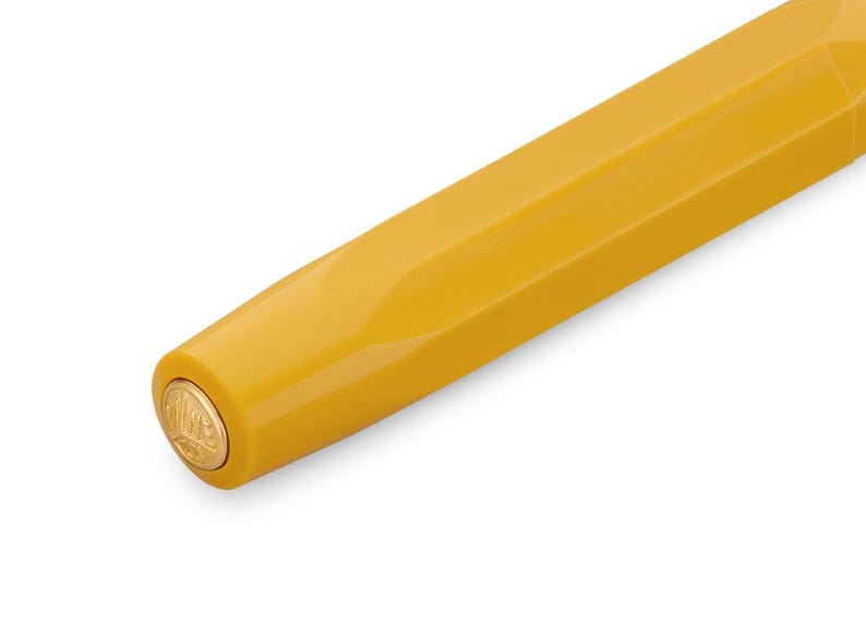 Op de afbeelding: Close-up van het uiteinde van een gele pen met een gouden dop met een logo.