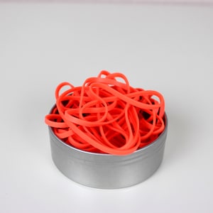 Könnte beinhalten: Ein Behälter gefüllt mit einer großen Menge leuchtend orangefarbener Gummibänder.