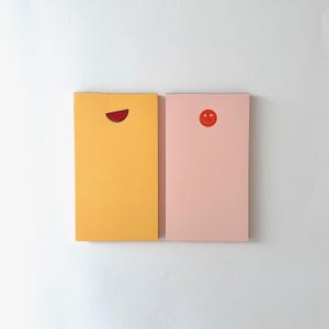 May include: Two rectangular notebooks. One is yellow with a watermelon slice graphic. The other is pink with a red smiley face graphic. Both notebooks are on a white background.