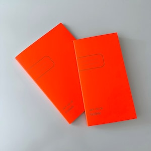 Puede incluir: Dos cuadernos de color naranja brillante con texto negro que dice "48 P. 100 GR" y "K107088058".