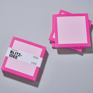 Könnte beinhalten: Ein Set quadratischer, leuchtpinker Haftnotizen mit weißem Raster. Ein Stapel ist mit einer weißen Papierbanderole versehen, auf der FOX & POET BLITZ-IDEE, 3 x 50 Blatt, 72 x 72 mm, Haftnotizen Leuchtpink steht. Ein zweiter Stapel liegt daneben.