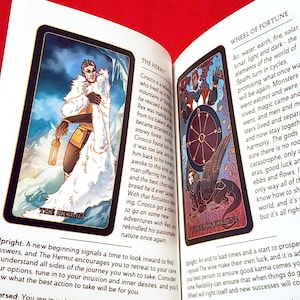 May include: Two tarot cards, The Hermit and Wheel of Fortune, with illustrations and descriptions. The Hermit card shows a man in a white hooded cloak standing in a snowy landscape. The Wheel of Fortune card shows a winged creature with a wheel in the center.